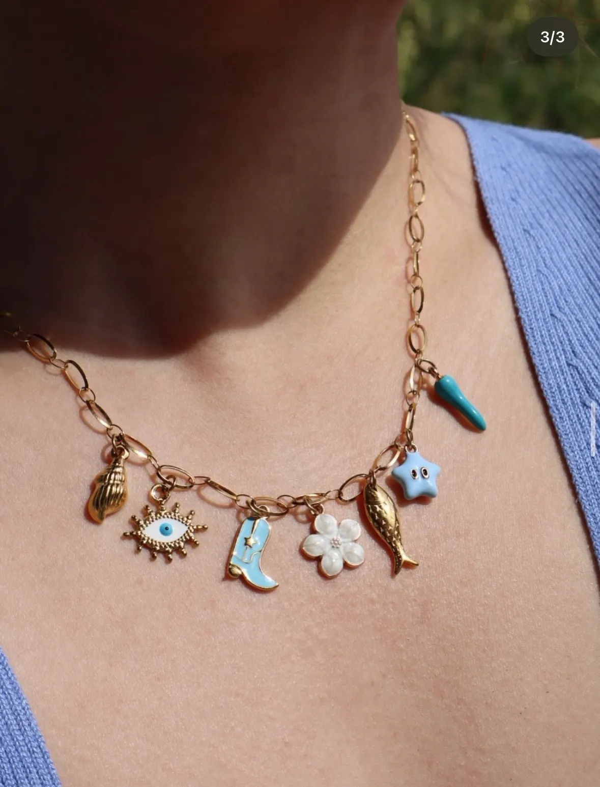 Collier à charms doré porté au cou — coquillage, œil turquoise, botte, fleur nacre, poisson et étoile émaillés